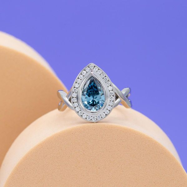A blue lab created diamond is surrounded by a white diamond halo and white gold band.