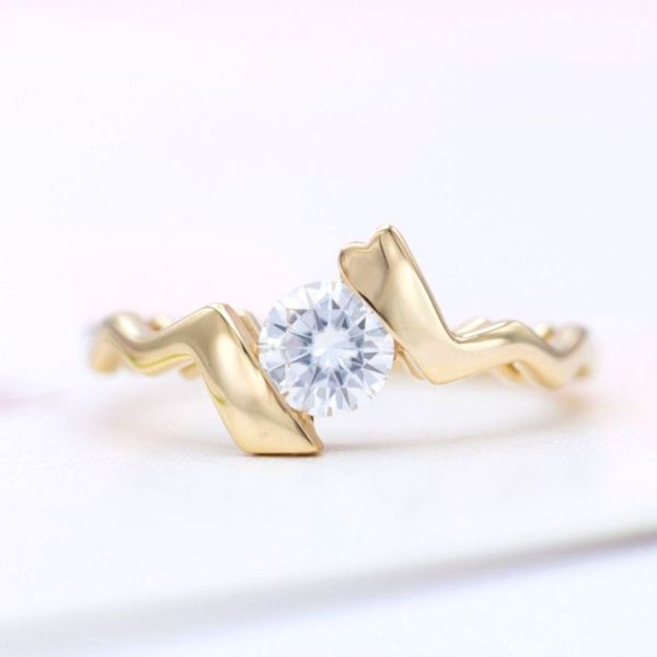 This uniquely shaped bypass engagement ring uses a tension-style setting to simulate the open, modern look but with a secure railing hidden under the center stone.