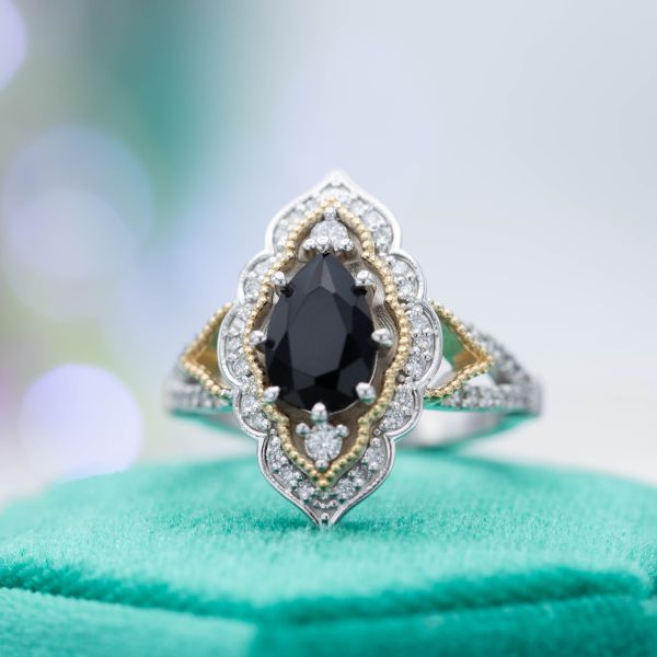 An elegant and bold vintage-inspired engagement ring surrounds a pear black diamond with a mixed yellow and white gold halo.