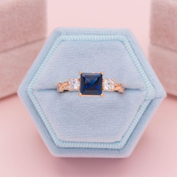 A lab created dark blue sapphire sits in the center of this rose gold engagement ring. Its princess cut brings out the dark blues of the center stone, and lab diamond accents add an extra touch of sparkle.