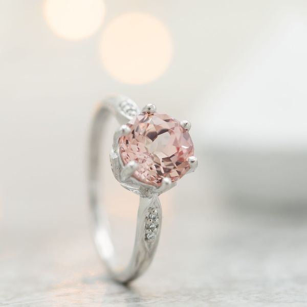 A delicate vintage-inspired engagement ring with a light, slightly peachy pink sapphire center stone.