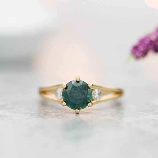A deep green sapphire engagement ring with a delicate, modern split shank and diamond side stones.
