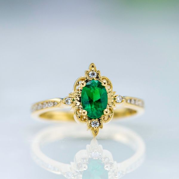 An oval emerald pairs with an intricate gold halo in the perfect vintage-inspired engagement ring.