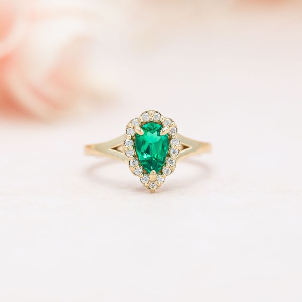 The pear shaped emerald in the center of this engagement ring has a yellow undertone.