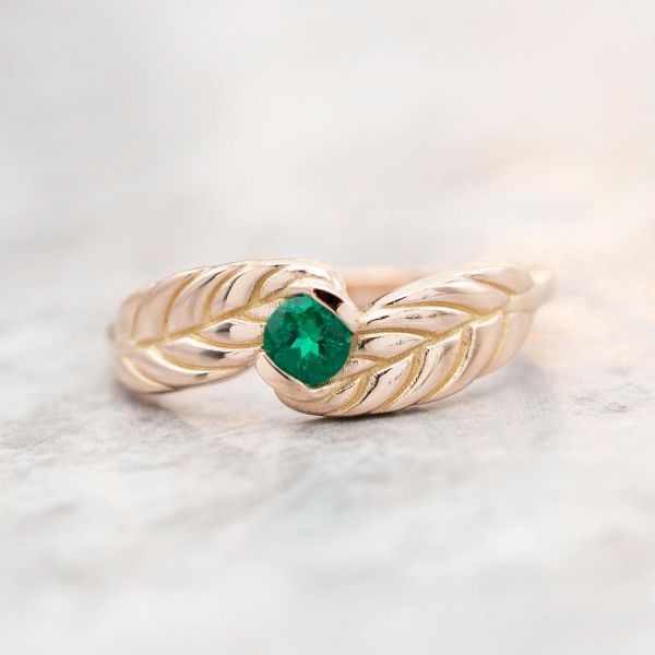 The rose gold band of this autumn-inspired engagement ring looks like leaves embracing the lab emerald center stone.