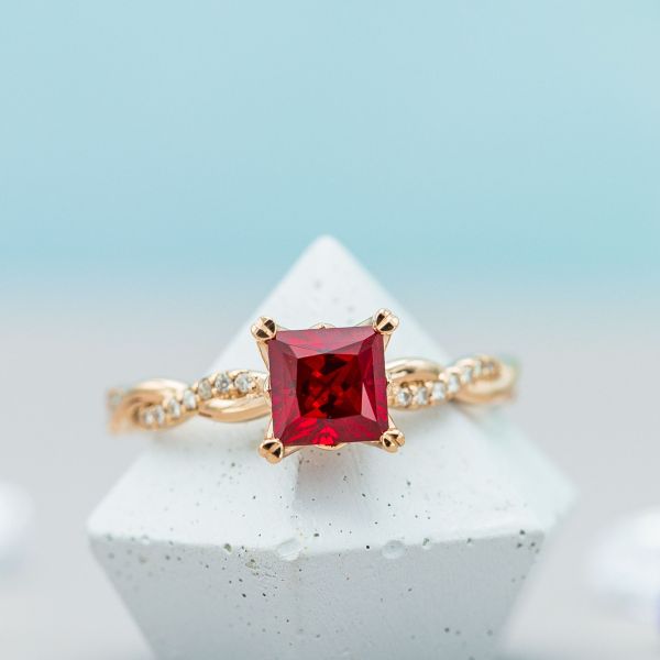 Princess cut ruby engagement ring with a vining rose gold and moissanite band.