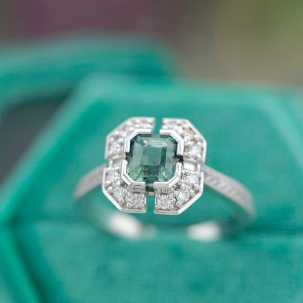 A unique Art Deco-inspired halo engagement ring with a blue-green sapphire.