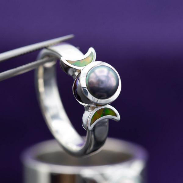 A black pearl surrounded by crescent moon opal inlays in this unique ring.