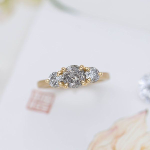 Salt and pepper diamonds sit in yellow gold in this three stone engagement ring.