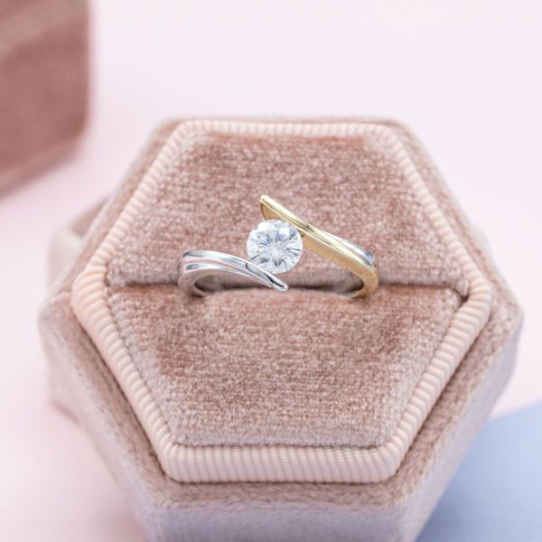 The sweeping lines of this two-tone white and yellow gold band make this engagement ring’s faux tension-set moissanite appear to float.