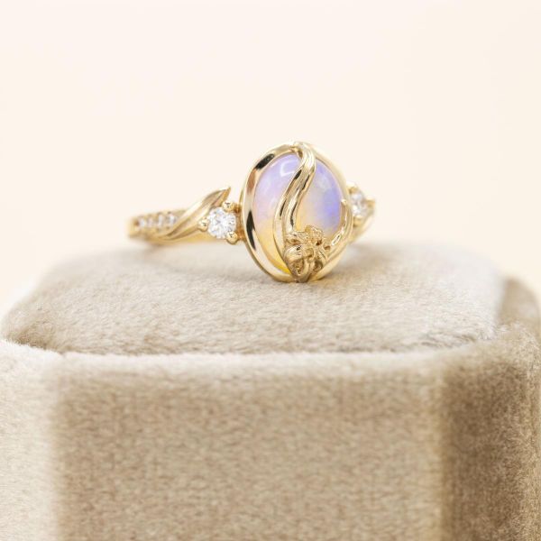 A floral white opal engagement ring with a gold vine extending over the face of the center stone.