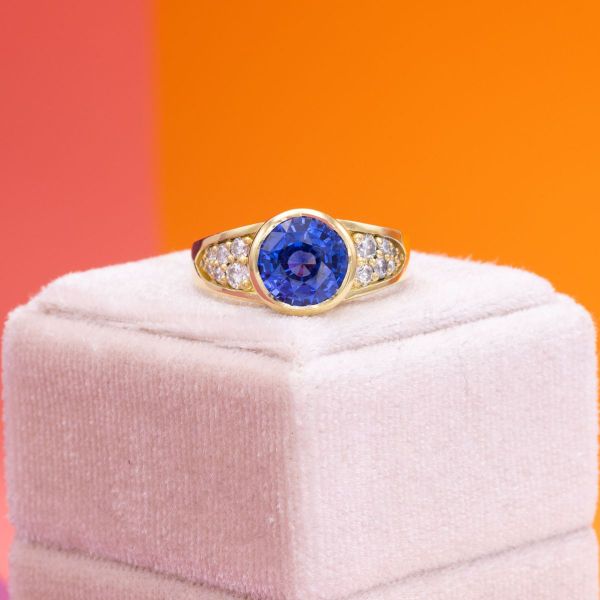 The yellow gold bezel positively glows against the dazzling blue of this sapphire ring. We drew out the essence of the bezel setting by filling the gaps of the dramatic split shank band with accent diamonds, with the overall effect creating a sparkling blue eye.