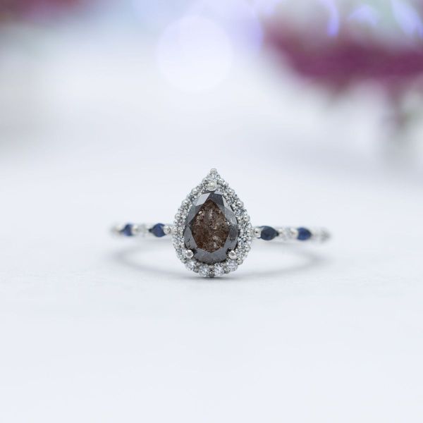 A pear cut salt and pepper diamond is surrounded by a white diamond halo.