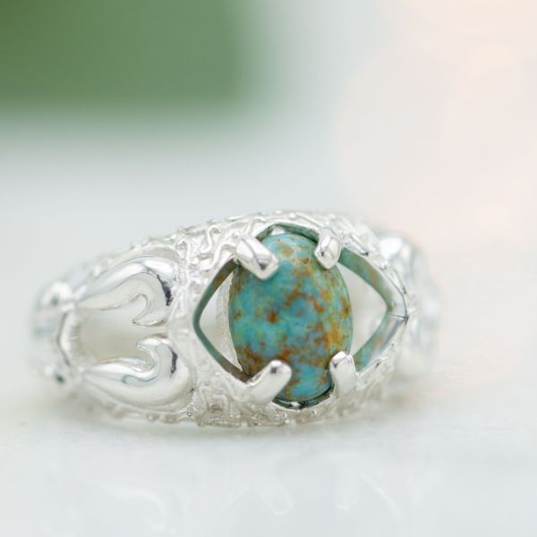 这枚大胆而独特的戒指的白金镶嵌与椭圆形蓝绿色中心石及其金棕色基质的丰富色彩形成对比。