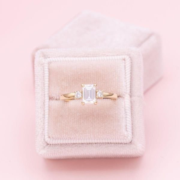 Three emerald cut moissanites sit on a yellow gold engagement ring band.