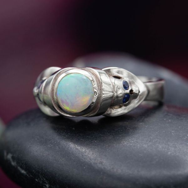 A classic skull ring form with the unusual play of pastel colors in the fire of the white opal center stone.