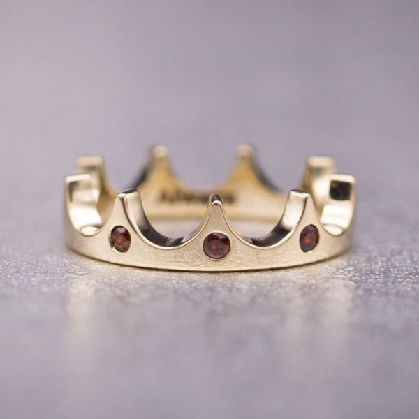 A truly regal rose gold crown ring with three flush-set garnet stones.