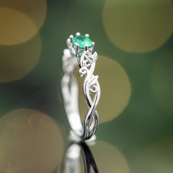 This east-west emerald engagement ring features a white gold flowery band.
