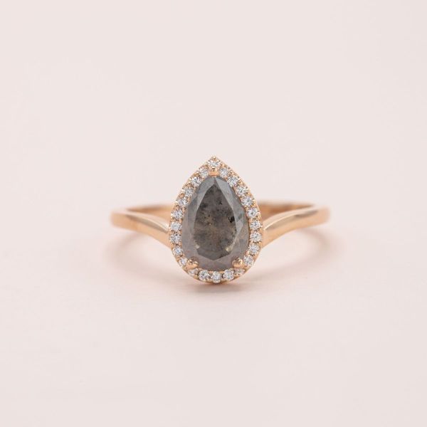A pear shaped salt and pepper diamond is held in yellow gold with a white diamond halo.
