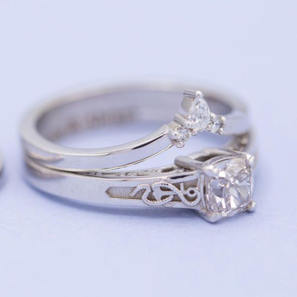 Two white gold tiara-shaped bands encompass a princess cut diamond on this anchor engagement ring.