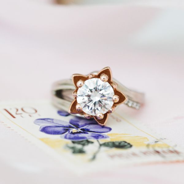 Inspired by her lotus tattoo, the center stone is set in two layers of rose gold petals, with a modern diamond-studded white gold shank.