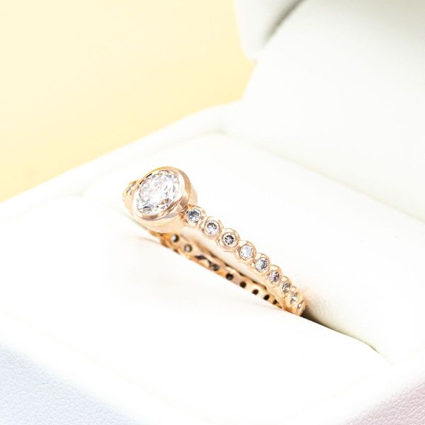 The pavé-set diamonds and center diamond of this engagement ring are wrapped in rose gold circles for a scalloped look.