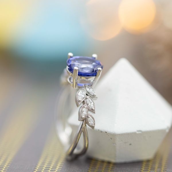 Delicate, leaf-lined engagement ring with oval blue sapphire and marquise diamond accents.