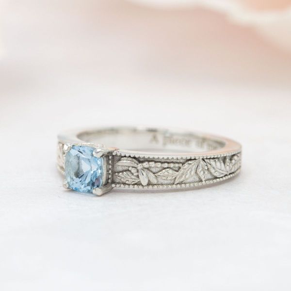This aquamarine ring has an intricate white gold band with engraved leaves and dragonflies.