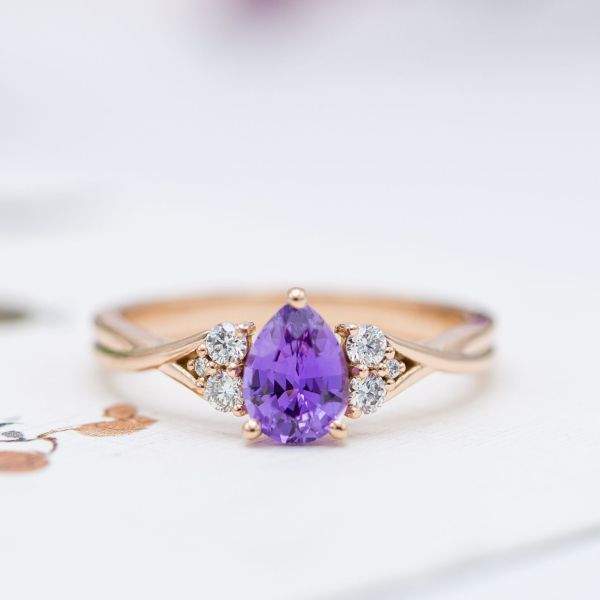 Purple sapphire engagement ring with diamond clusters and a twisting rose gold band.