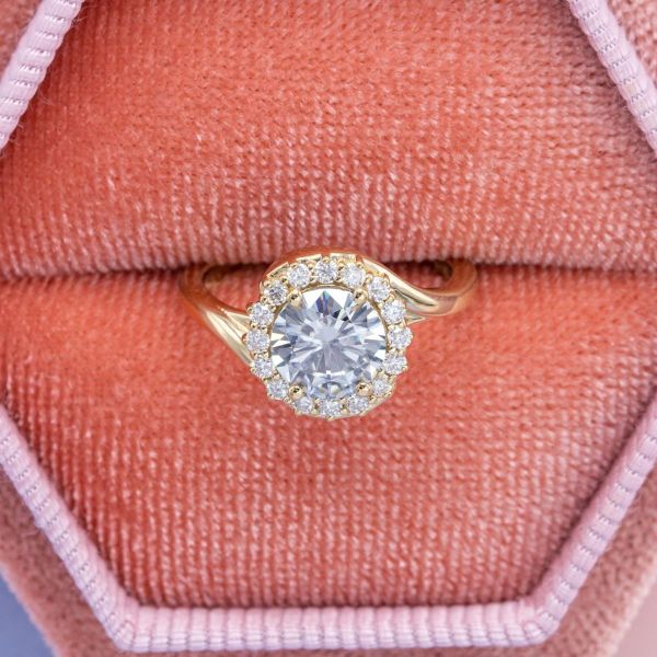 A round brilliant moissanite sits in the center of a halo engagement ring.