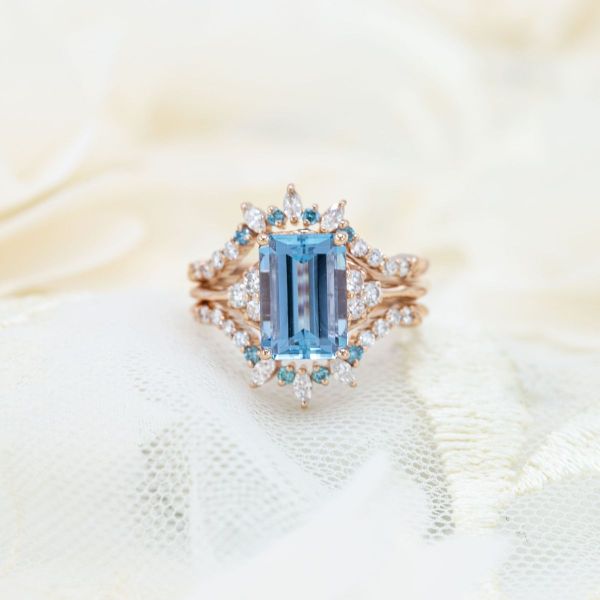 This emerald cut aquamarine is surrounded by a starburst of accent diamonds and sapphires.