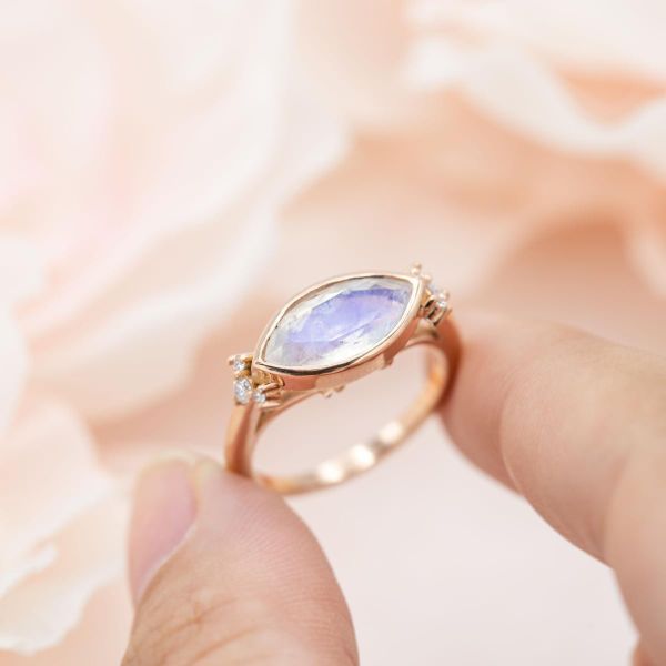 Marquise moonstone engagement ring with an east-west bezel setting and accent diamonds.
