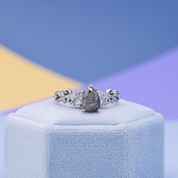 A dark gray salt and pepper diamond in a pear cut is held in white gold.