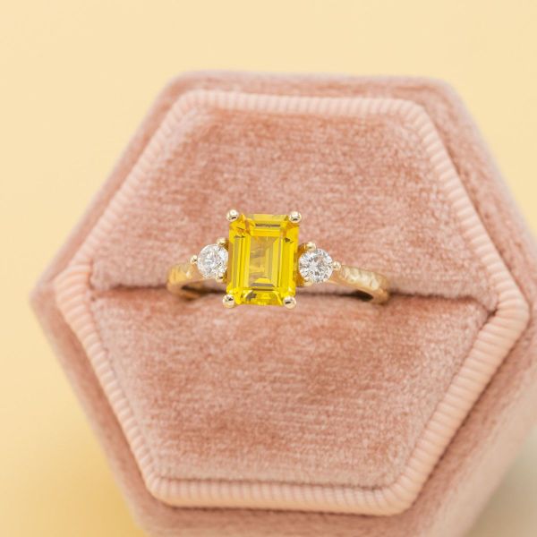 A yellow, emerald cut sapphire in a yellow gold setting with diamond accents.