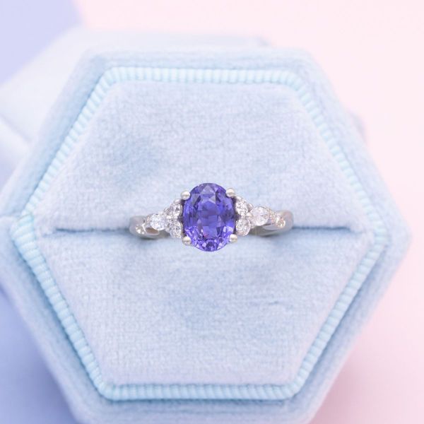 An oval cut purple sapphire sits in the center of diamonds on this white gold engagement ring.