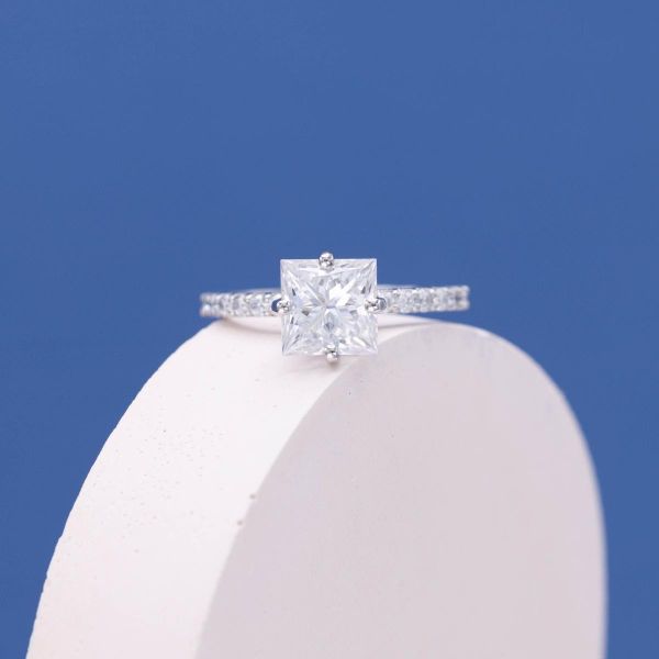 An icy white princess cut moissanite engagement ring with a pave band.
