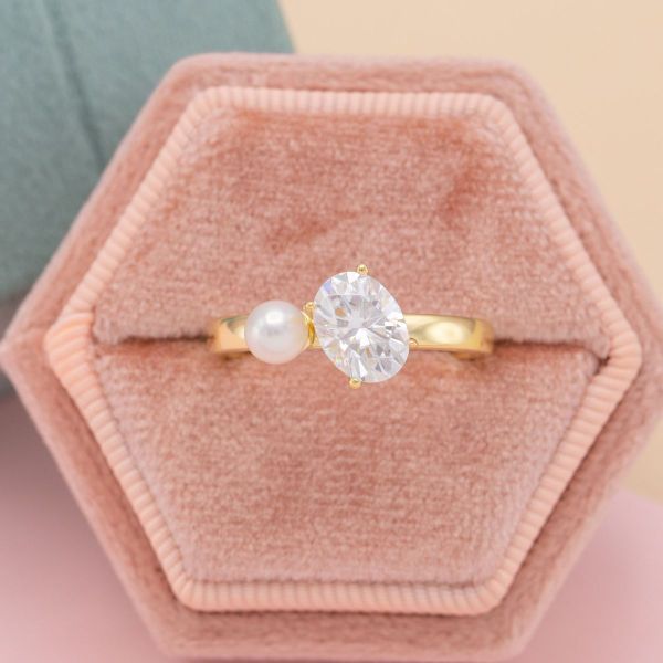 A pearl and oval cut moissanite sit in the center of this yellow gold toi et moi engagement ring.
