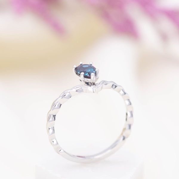 The white gold band of this engagement ring resembles braided rope with a pear-shaped alexandrite hanging at the center.