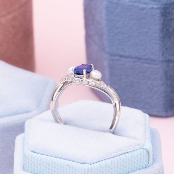 A vibrant blue sapphire center stone is surrounded by snowy white pearls, inspired by winter florals.