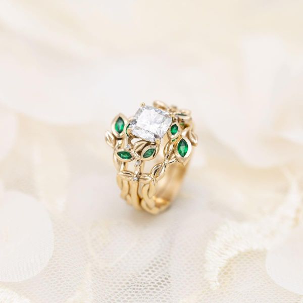 A bold three-ring engagement and wedding band set with emerald leaves and gold vines surrounding a cushion cut diamond.