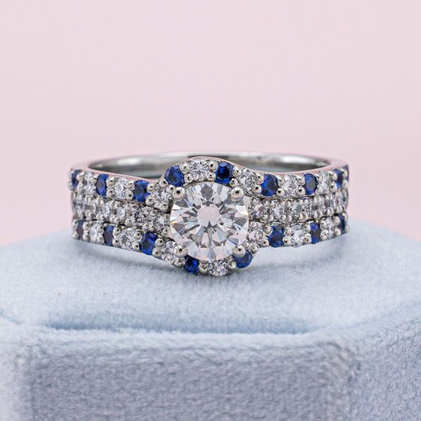 The dazzling sparkle of this diamond and platinum engagement ring is taken to new heights when paired with the sapphire and diamond wedding bands. The pops of deep blue add depth and interest, especially in the way they wrap around the slightly offset band of the engagement ring.