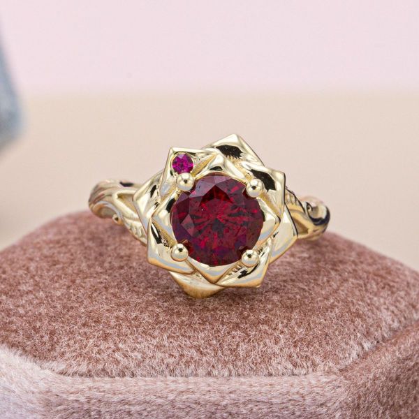 A deep red ruby sits in a bold yellow gold rose petal setting to create a stunning rose engagement ring.