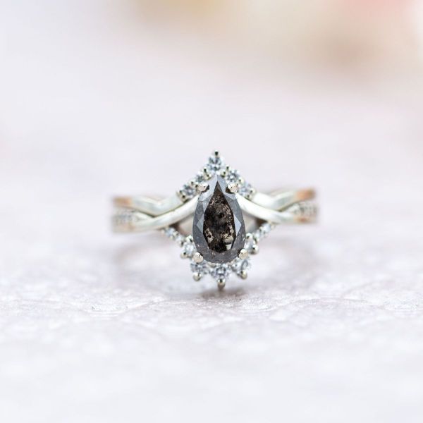 A mesmerizing pear cut salt and pepper diamond centers this regal bridal set with diamond accents on white gold bands.
