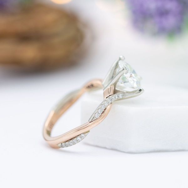 This moissanite centered engagement ring sits on an interlacing rose and white gold band, one section of band with pavé-set moissanites.