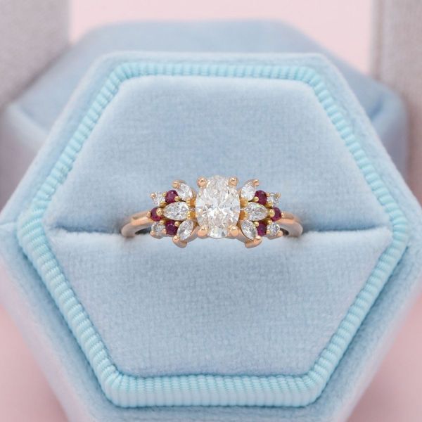 A spray of rubies and diamonds make a symmetrical cluster frame around the oval diamond in the center of this ring.