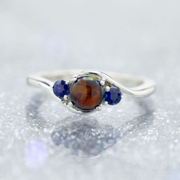 Sleek curves in this three-stone bypass setting, with the atypical pairing of blue sapphire and black opal.