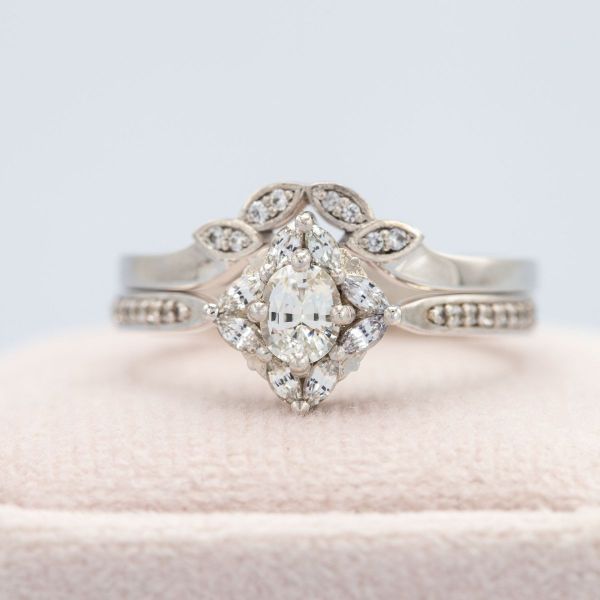 Who says diamonds are the only colorless stone you can use in an engagement ring? This white gold bridal set boasts an oval cut white sapphire at the center of the engagement ring, framed by a halo made of marquise cut white sapphires. And on the wedding band? You guessed it; more white sapphires for even more bling!