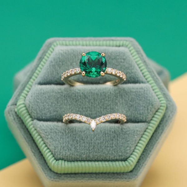 This engagement ring is blinged out with pavé-set diamonds highlighting a round cut emerald and more pavé-set diamonds on the matching wedding band.
