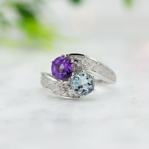 Amethyst and aquamarine sit in a toi et moi setting with diamond accents,.