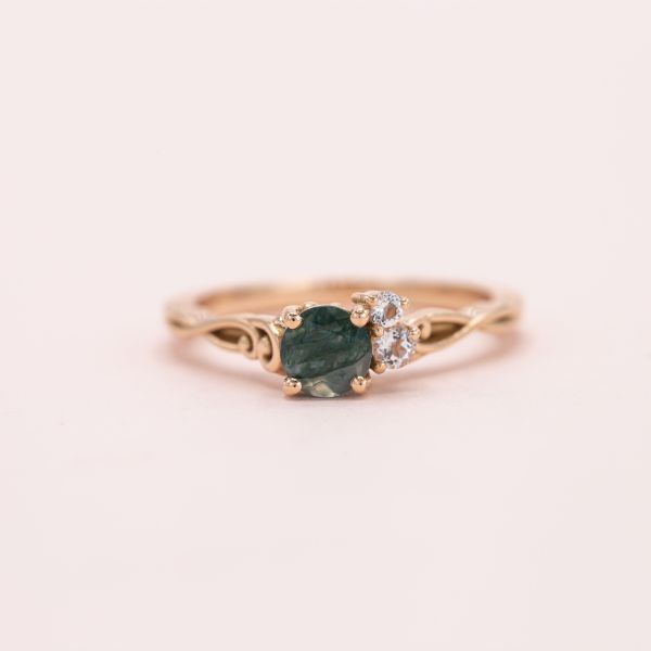 Curvy, asymmetrical engagement ring in rose gold with a cluster of dark green moss agate and diamonds.
